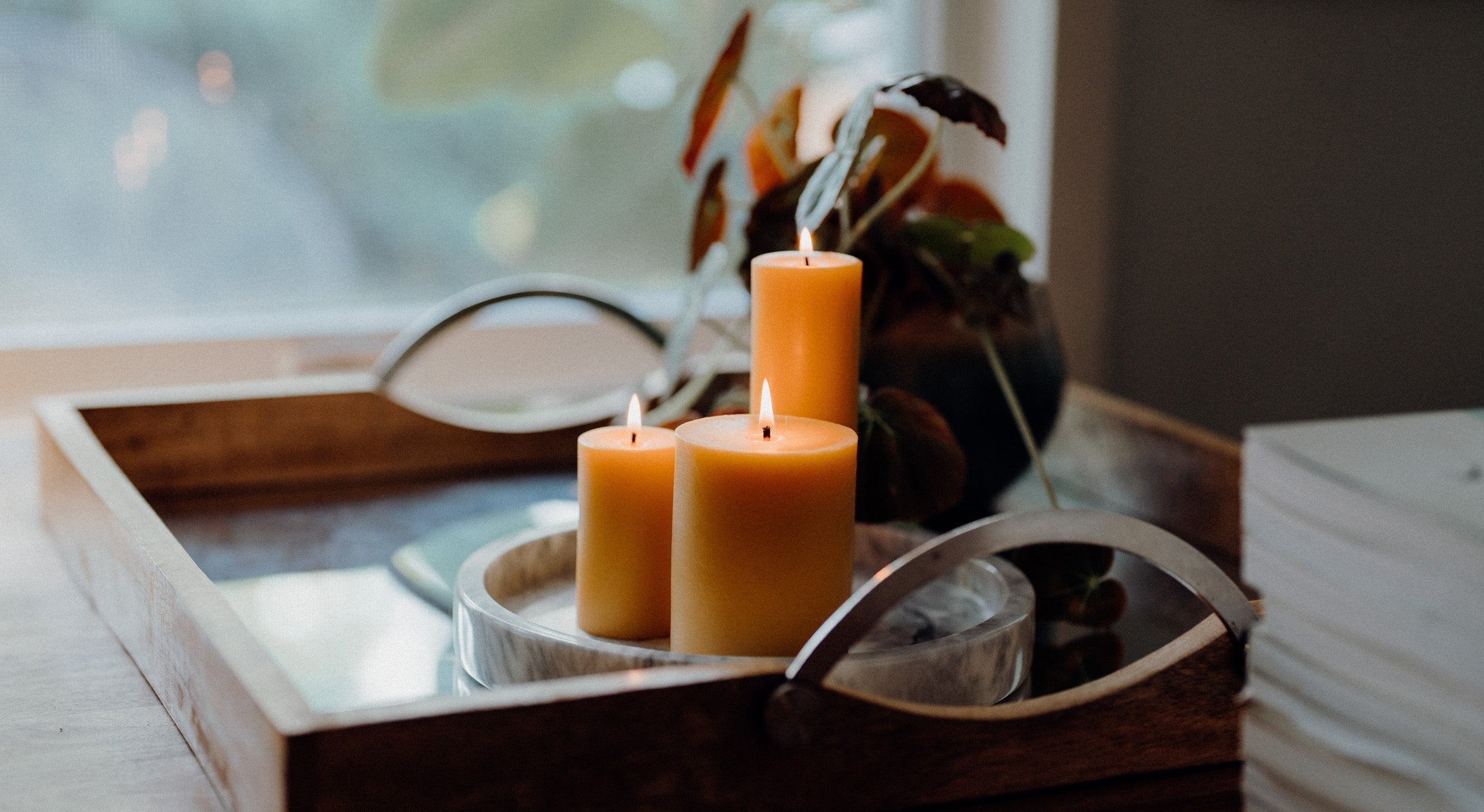 Three lit beeswax pillars on a wood tray