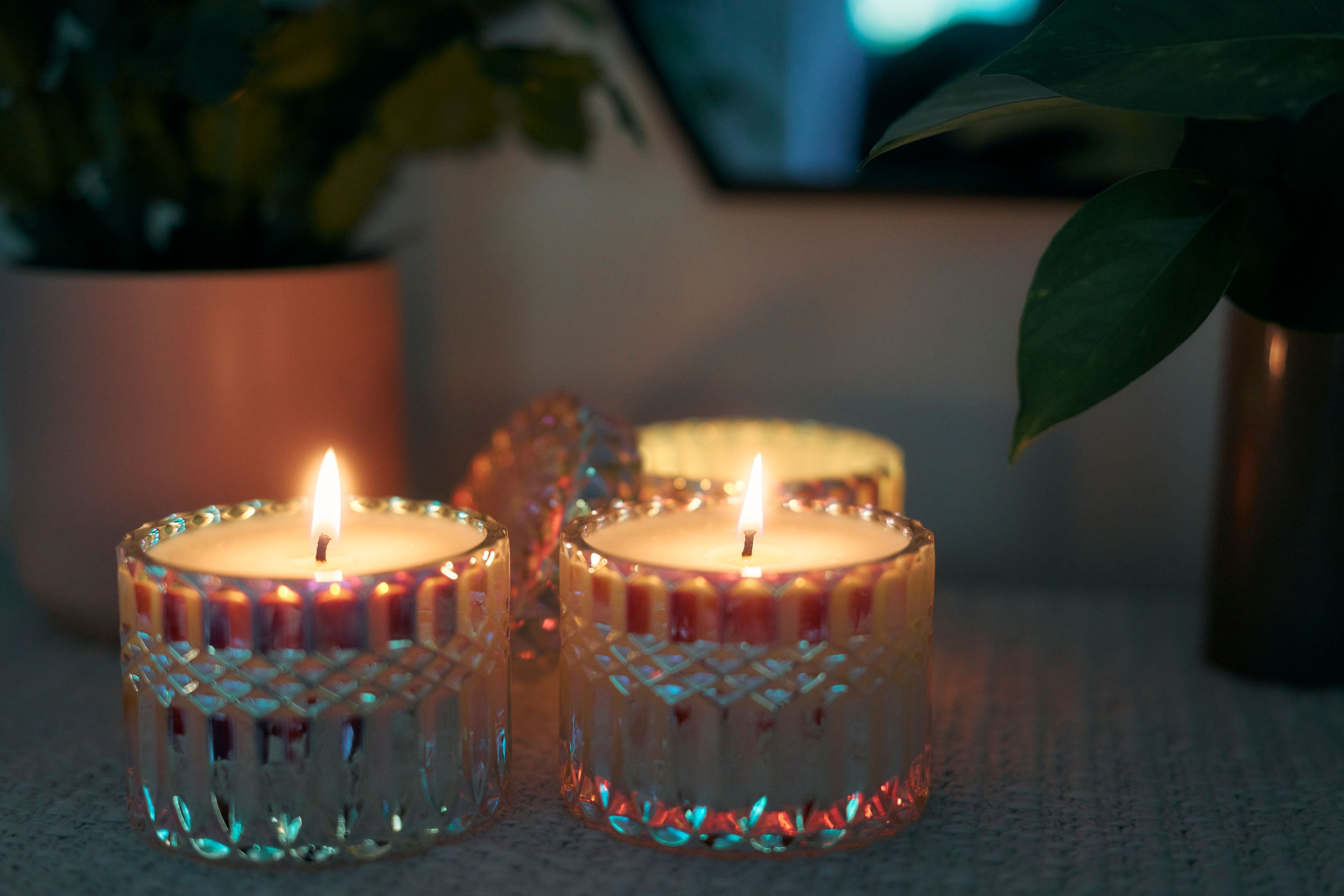Sunbeam Candles SunCatcher scented apricot, coconut & soy wax iridescent container candles lit on a table in a dark room with plants behind them