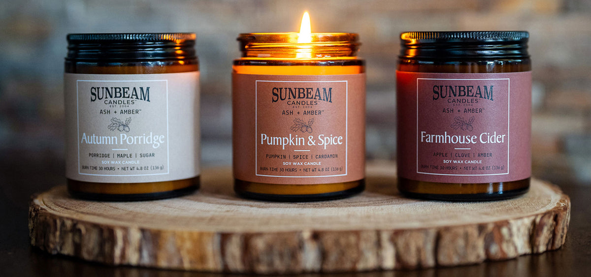 3 Ash + Amber soy jar Fall themed candles on a cross section of a tree - the middle one is lit