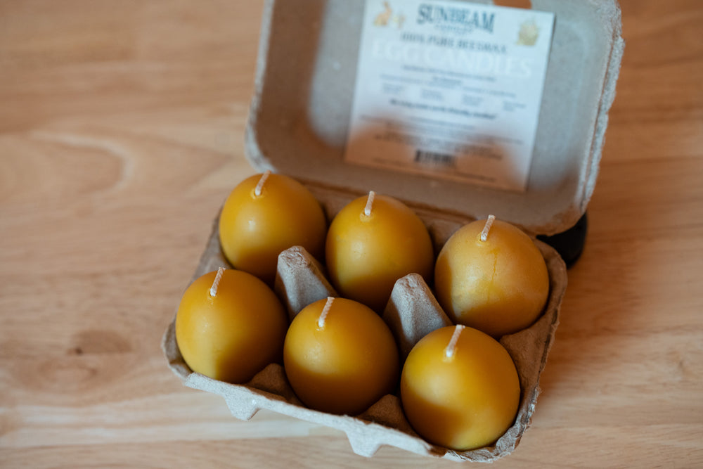 Yellow candles in an egg carton on a wooden surface with 'Sunbeam' branding.