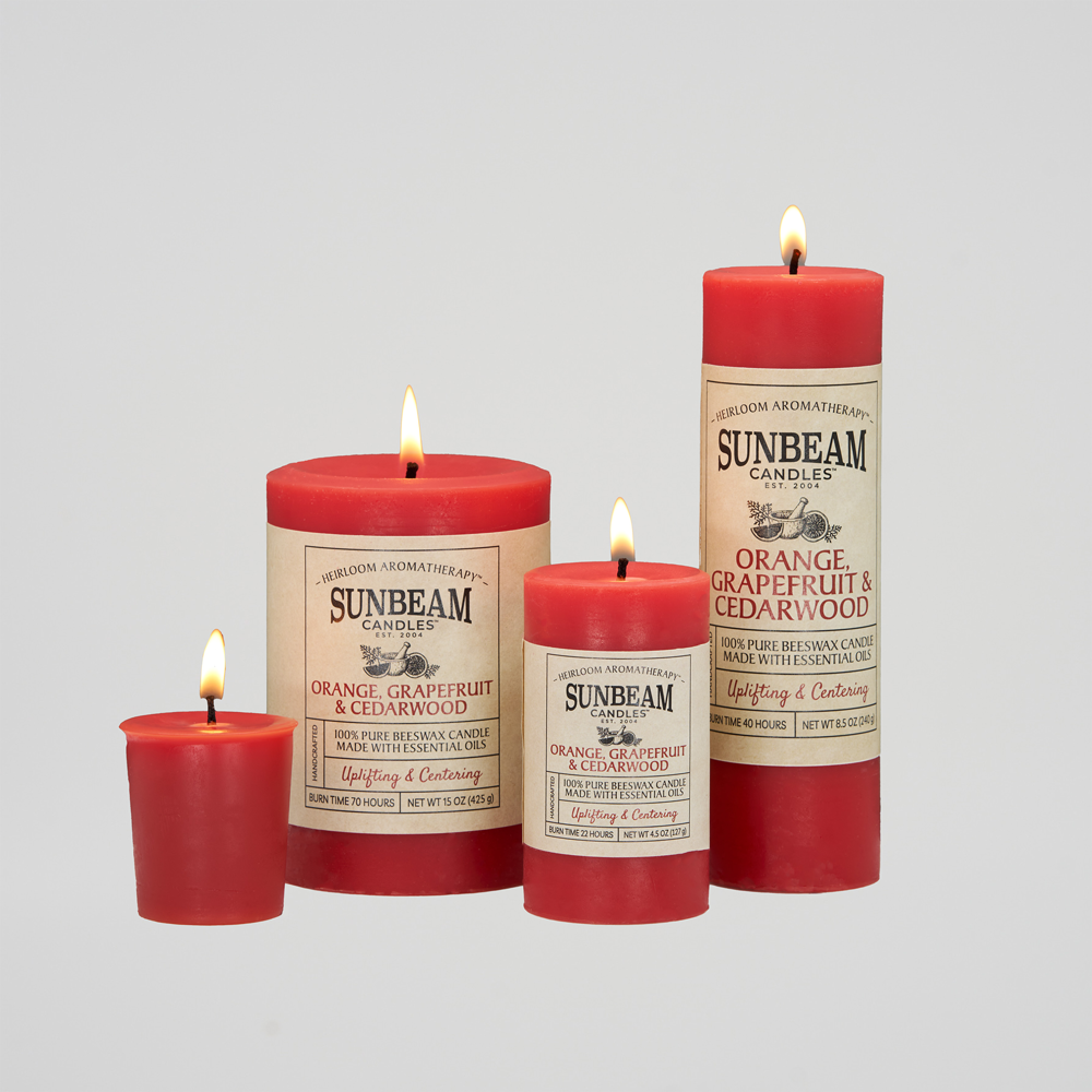 Sunbeam Candles Pure Beeswax lit reddish-orange Orange, Grapefruit & Cedarwood pillar and votive candles with white background