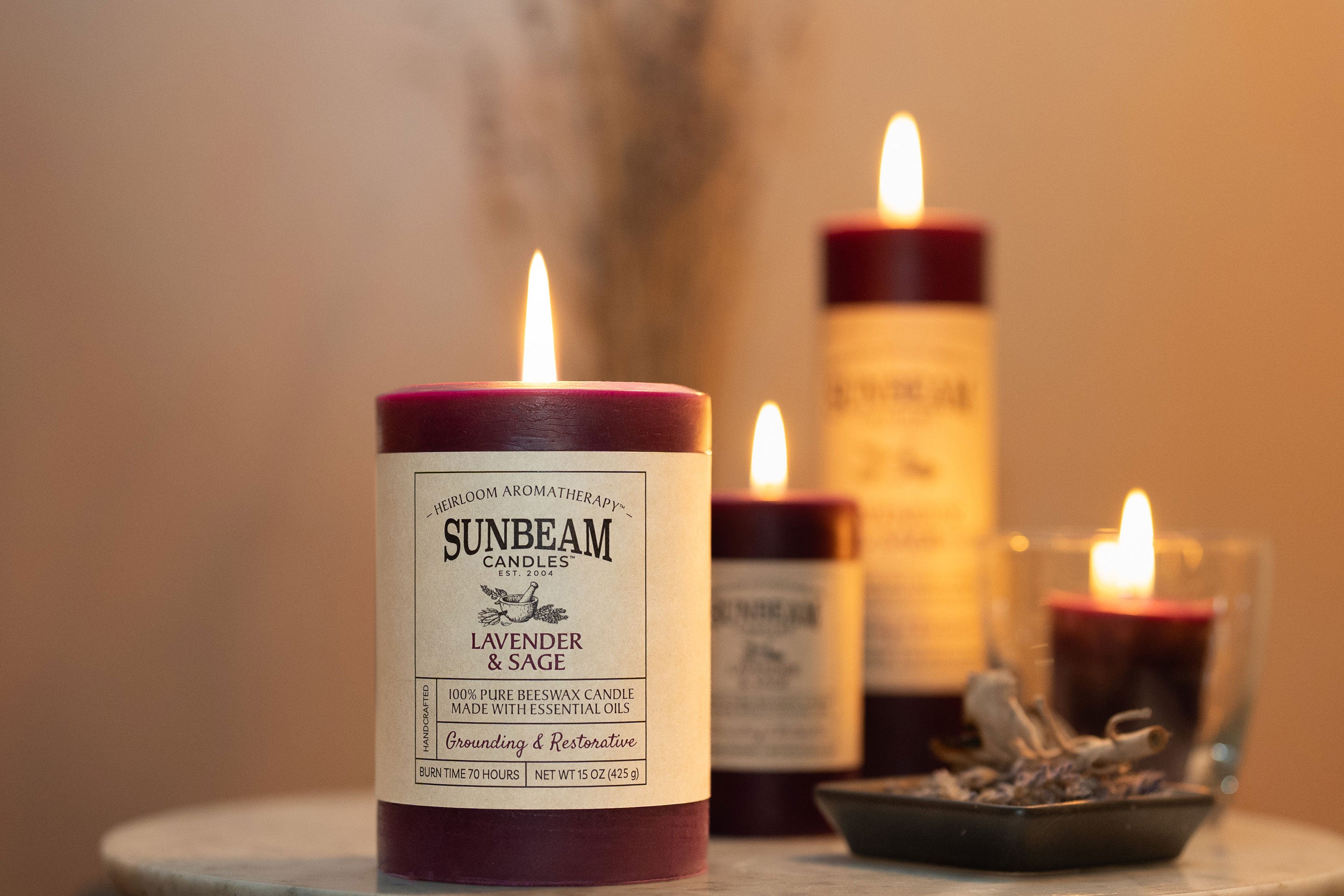 Sunbeam Candles purple Pure Beeswax Lavender & Sage lit pillar and votive candles on a table with sage in a dish