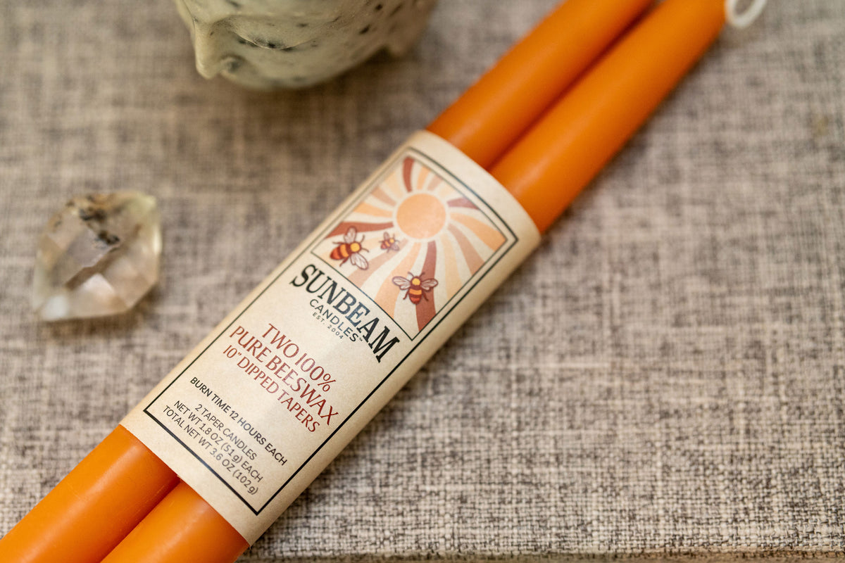 One pair of Sunbeam Candles 10" Dipped Beeswax Apricot Tapers with a label wrapped around sitting on a grey surface with a crystal next to it.