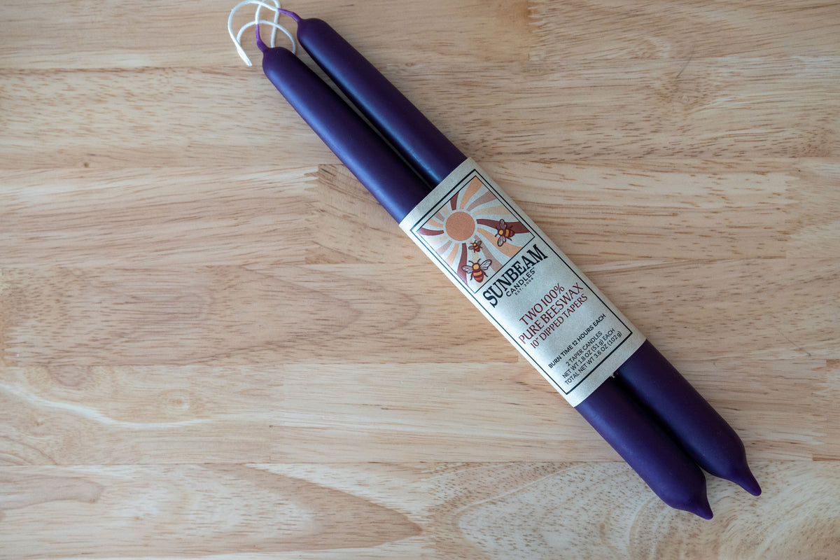One pair of Sunbeam Candles 10" Dipped Beeswax Plum Tapers with a label on a wood table.