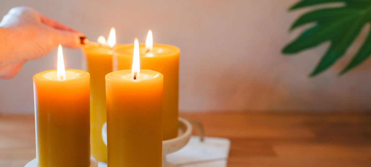 Three lit Sunbeam Candles Smooth Natural Gold Pillar candles on a wooden surface with a blurred background