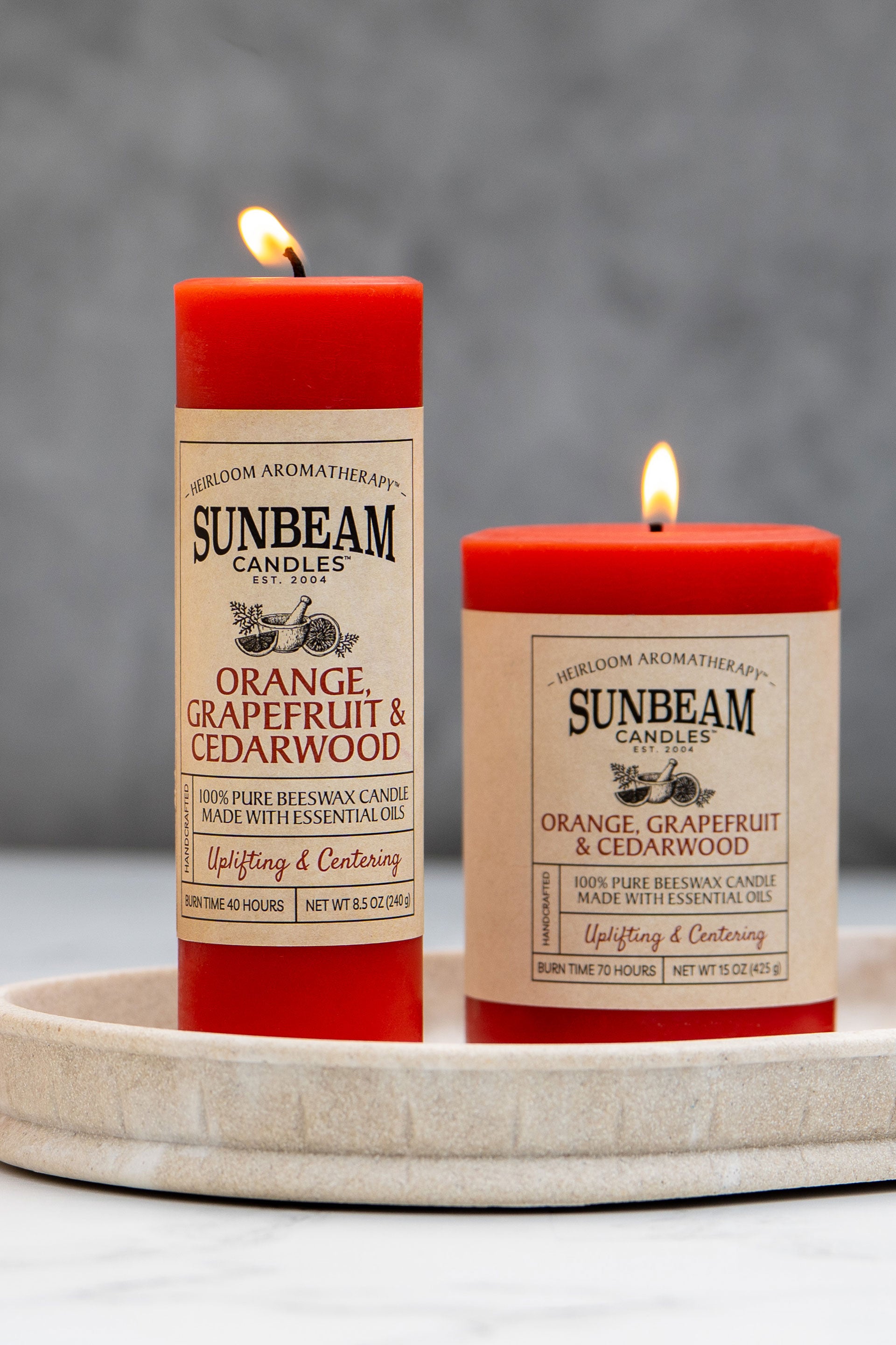 Sunbeam Candles Pure Beeswax reddish-orange Orange, Grapefruit & Cedarwood pillar candles in a dish with a grey background