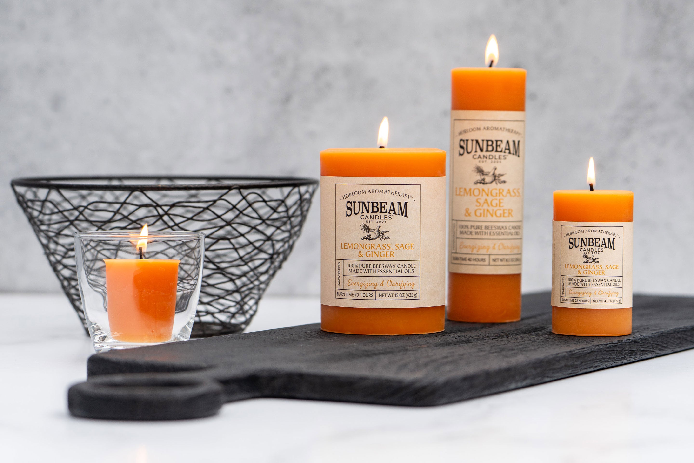 Sunbeam Candles Pure Beeswax saffron Lemongrass, Sage & Ginger pillar and votive candles on a cutting board with a grey background and metal bowl behind them
