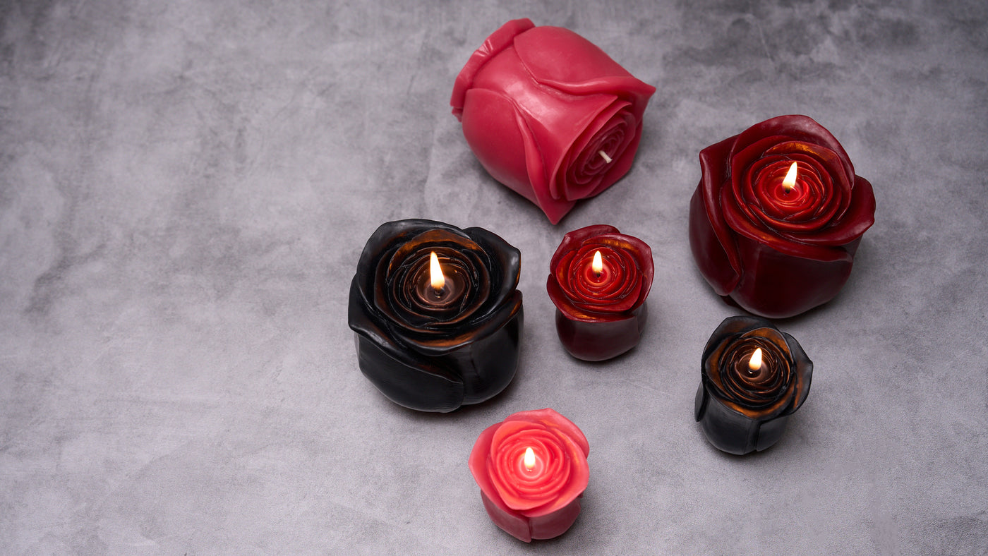 Two rose candles burning on a table with flowers