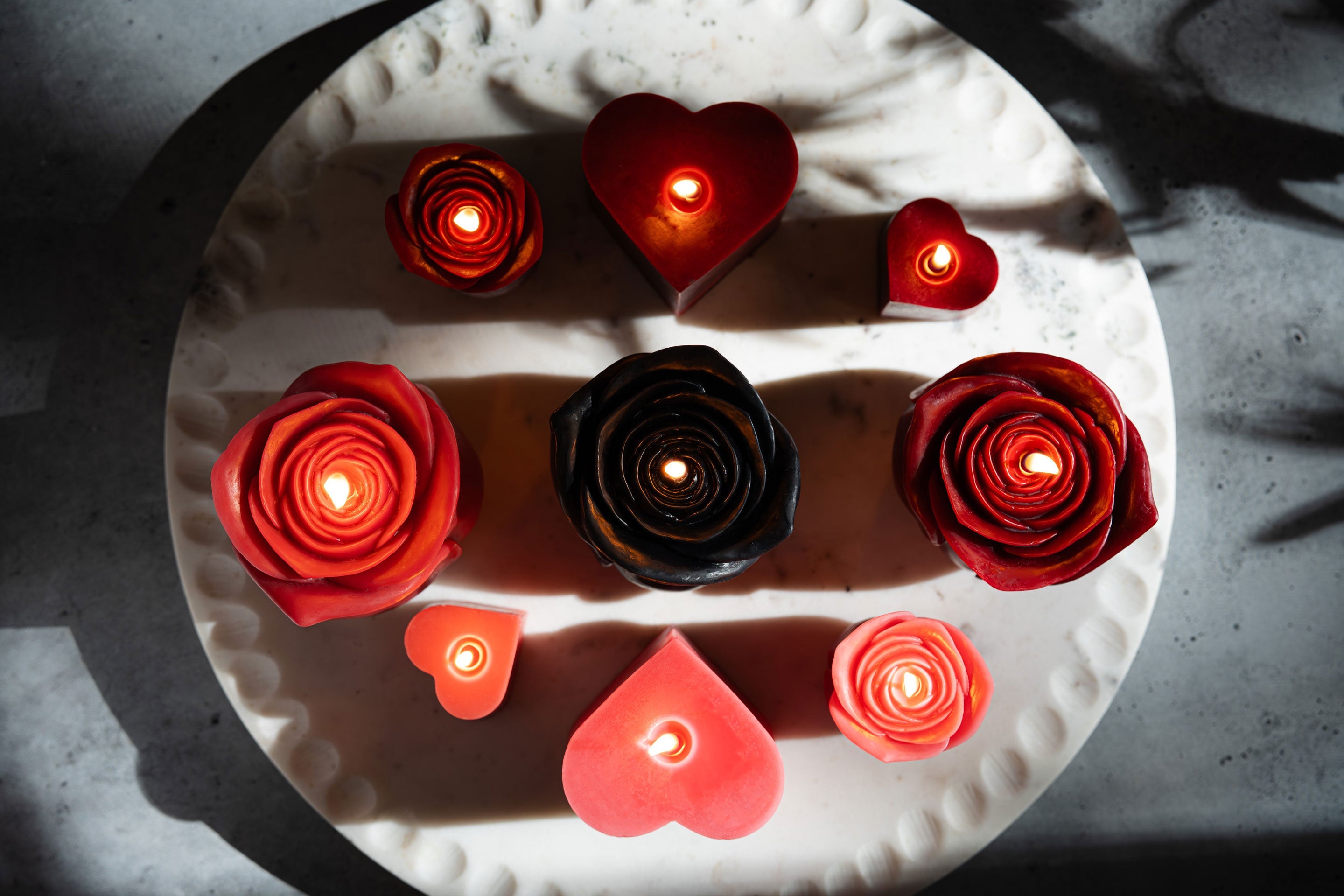 Sunbeam Candles various pure beeswax red, black & pink heart and rose candles lit on a white plate with shadows, view from above