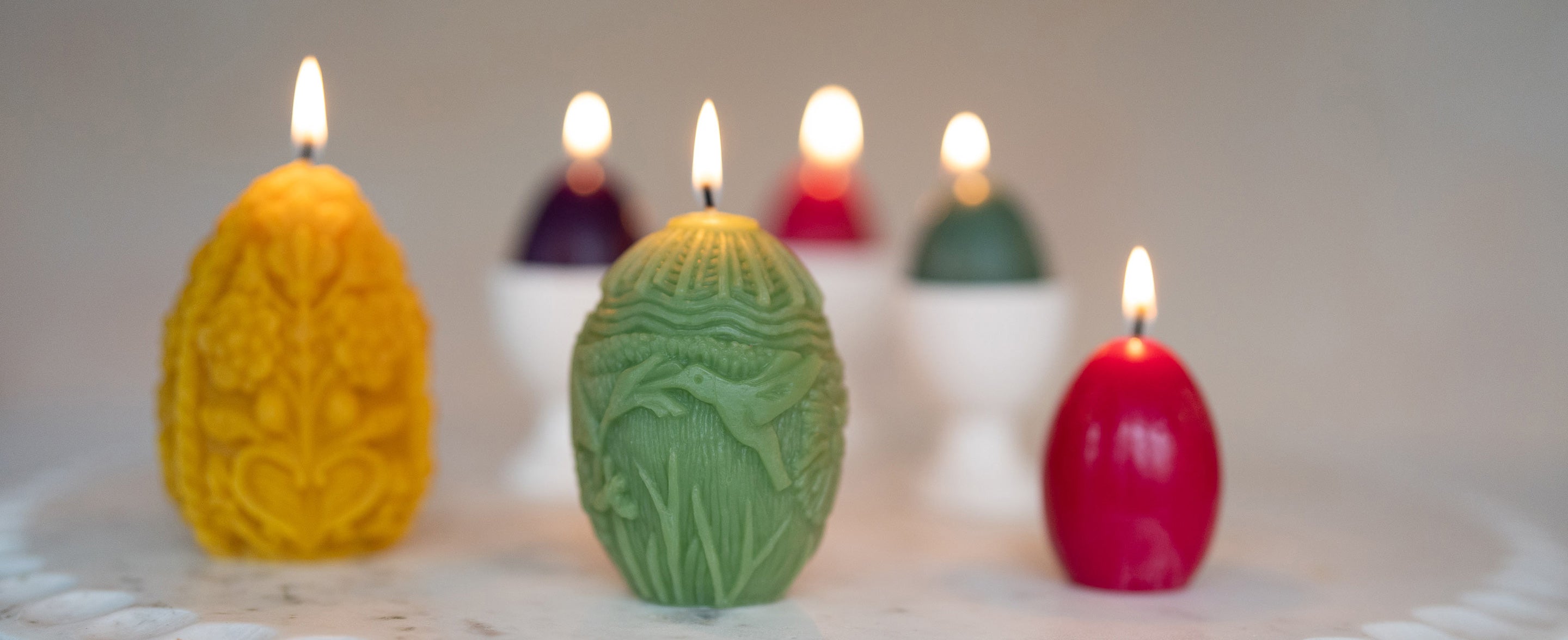 Sunbeam Candles various pure beeswax egg candles lit on a marble tray on a white table surface
