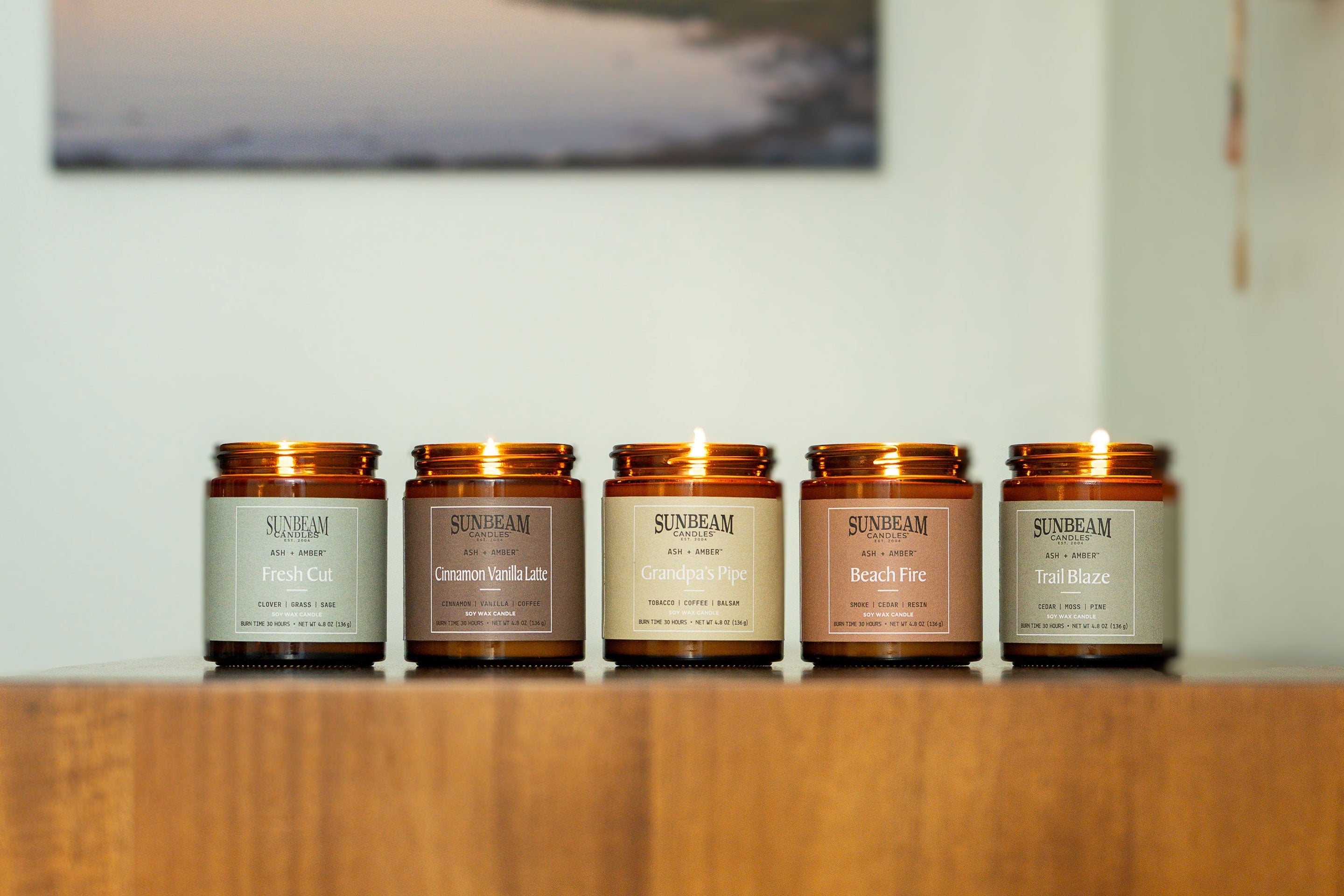 Sunbeam Candles Everyday Scent Ash + Amber soy wax jar candles on a table with a painting behind them on an off-white wall