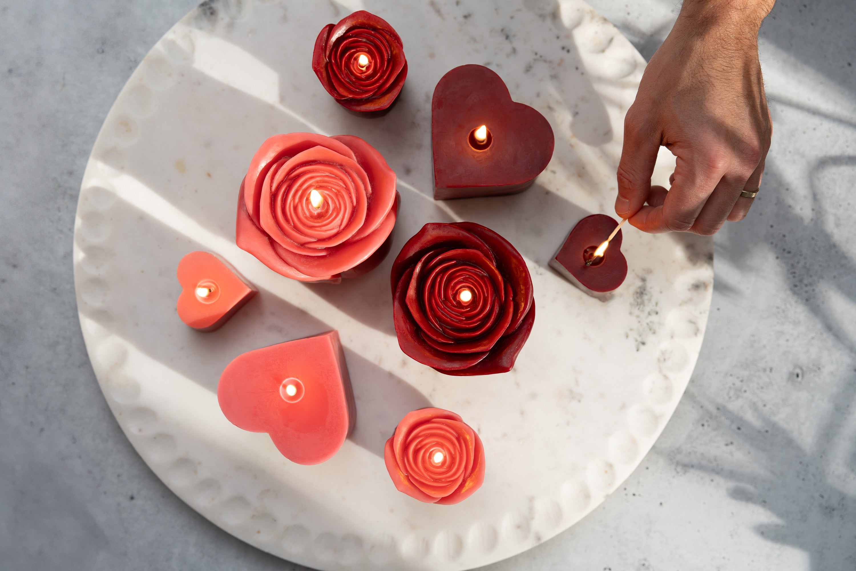 Sunbeam Candles various pure beeswax red and pink heart and rose candles being lit by a hand on a plate on a white surface