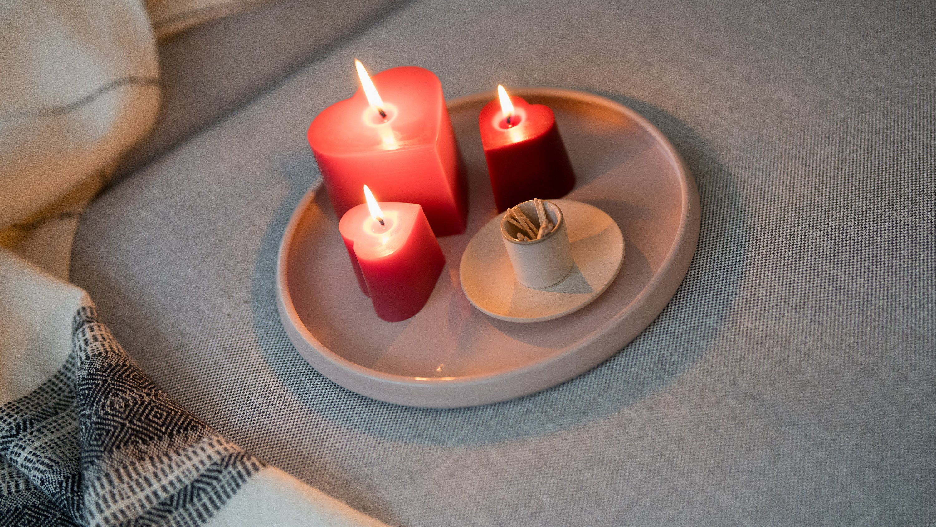 Sunbeam Candles Pure Beeswax Red & Pink Heart Candles lit on a dish sitting on a grey couch.