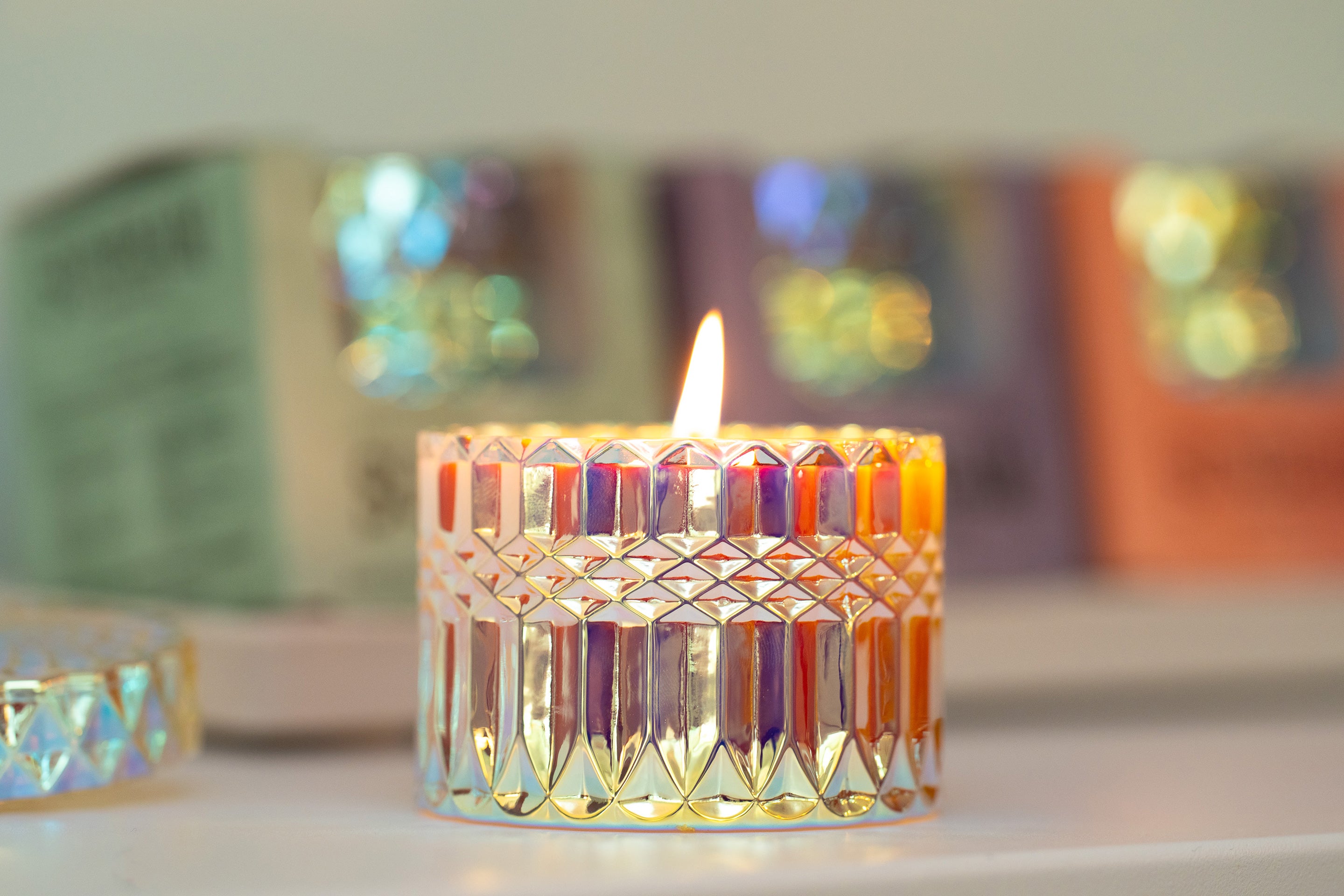 Sunbeam Candles SunCatcher scented apricot, coconut & soy wax iridescent container candle lit with boxed SunCatcher candles and a lid blurred in the background
