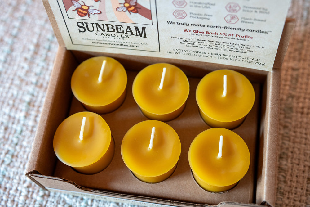 Box of Sunbeam candles with six yellow candles inside, on a textured surface.