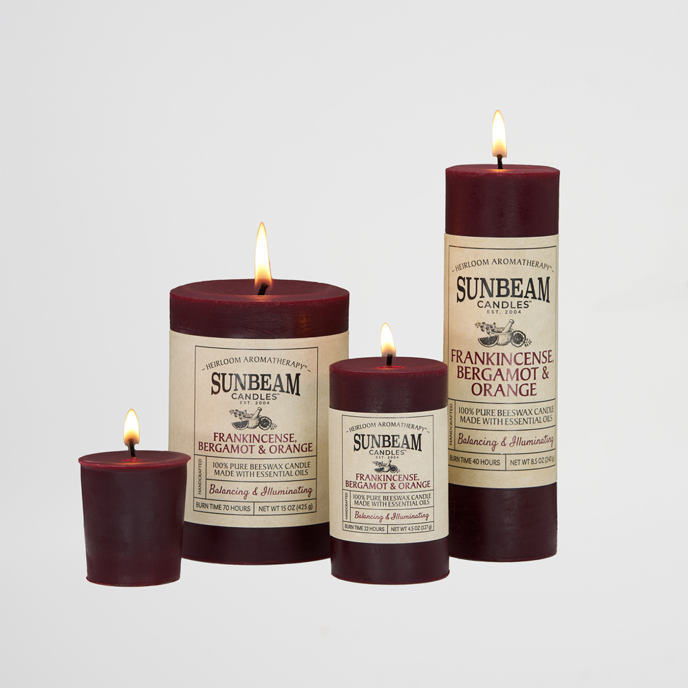 Sunbeam Candles  Pure burgundy Beeswax Frankincense Bergamot & Orange lit pillar candles in various sizes on a white background