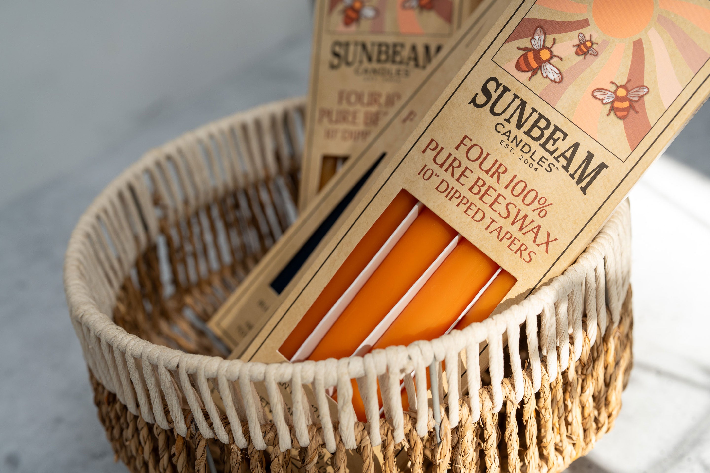 Sunbeam Candles 10" Dipped Beeswax Tapers in boxes sitting in a woven basket on a light background