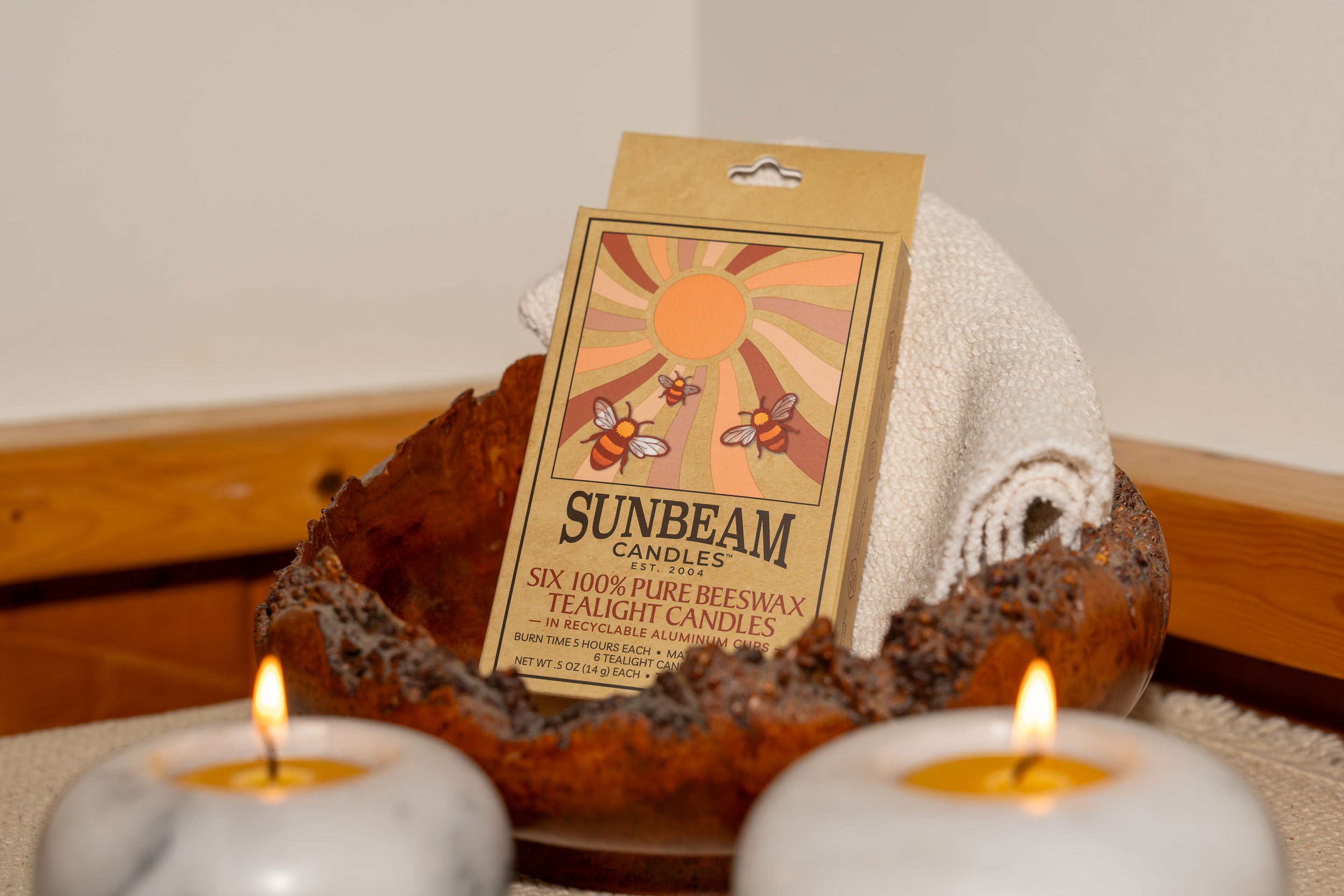 Sunbeam Candles 100% pure beeswax tealight candles in a 6-ct case sitting in a dish with two lit tealights in holders in front.