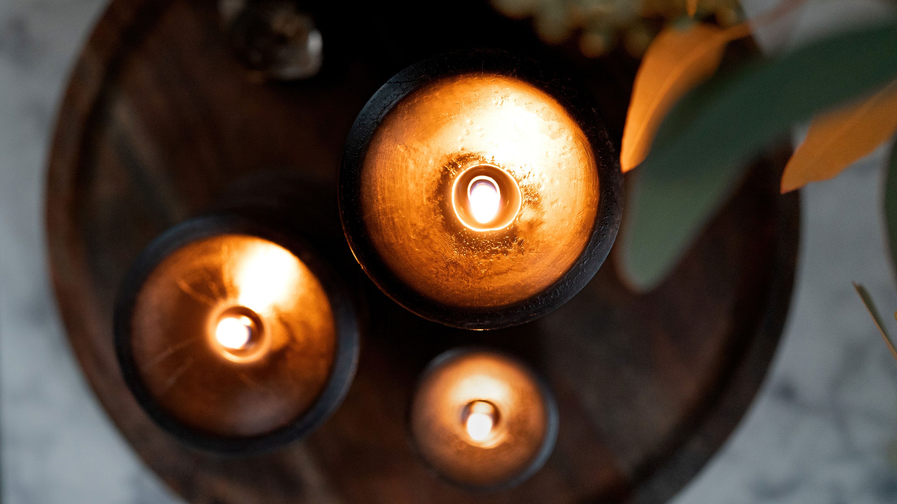 Three Sunbeam Candles Smooth Midnight Black Beeswax Pillars lit on a wood tray shot from above.