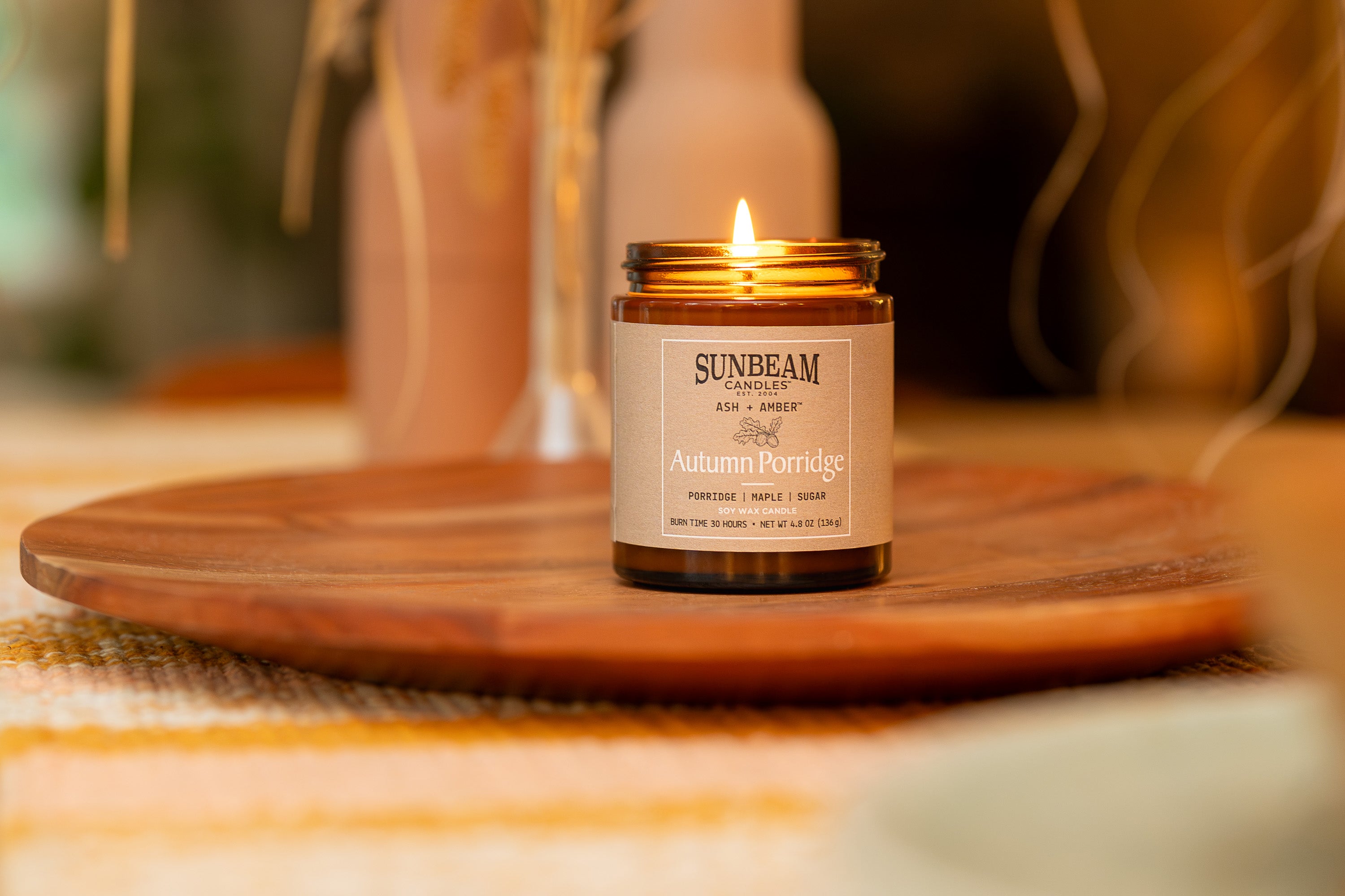 Sunbeam Candles Ash + Amber Fall Scent Autumn Porridge soy wax jar candle on a wood plate with a blurred background