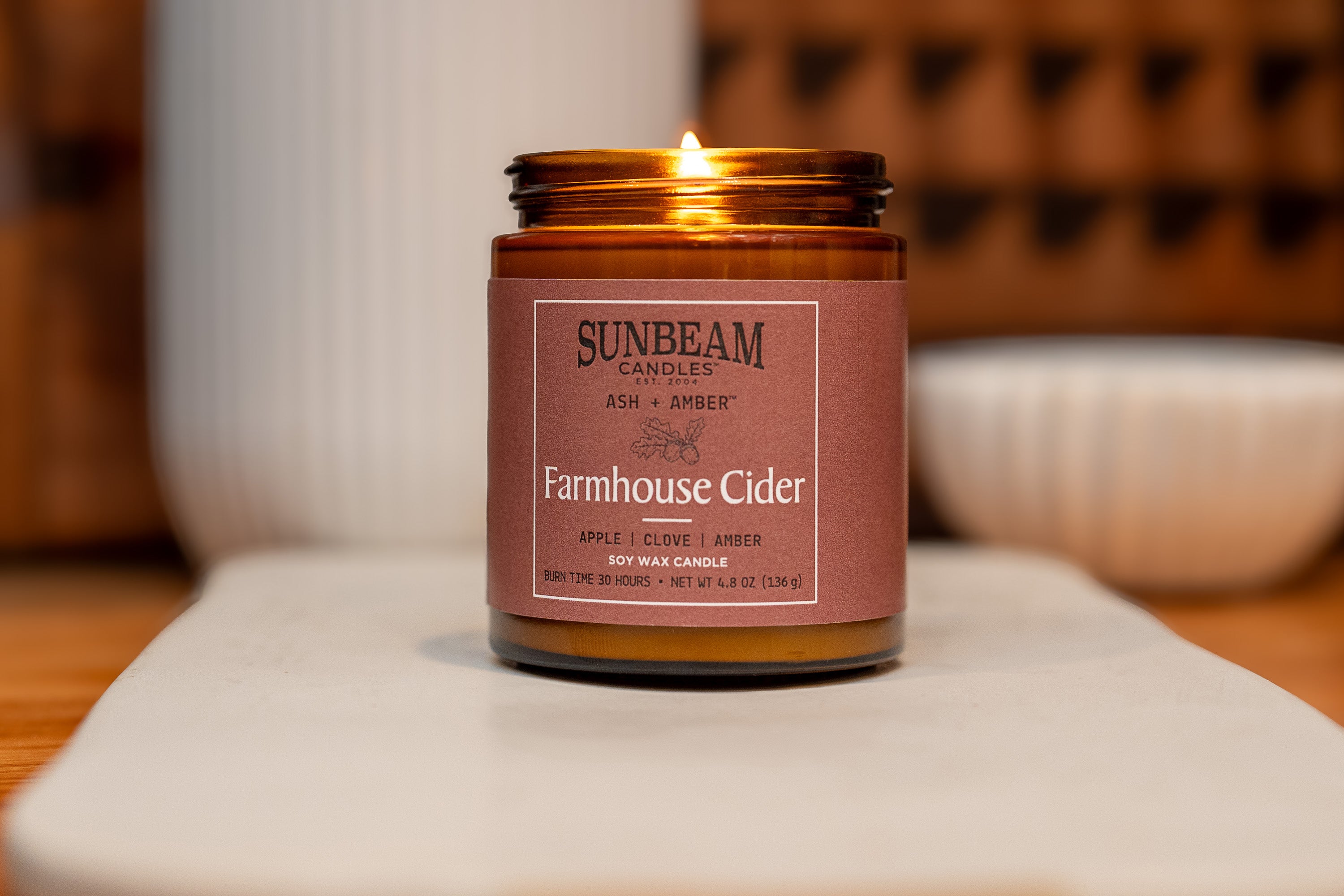 Sunbeam Candles Ash + Amber Fall Scent Farmhouse Cider soy wax jar candle on a tray with a blurred background