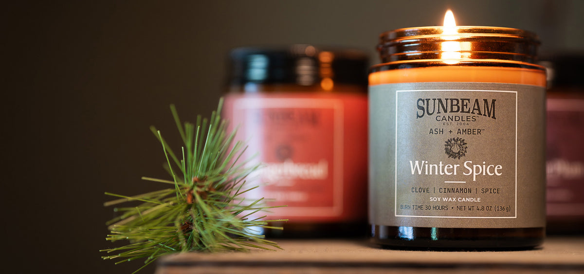 Ash + Amber soy jar candles lit on a shelf with a pine leaf next to them