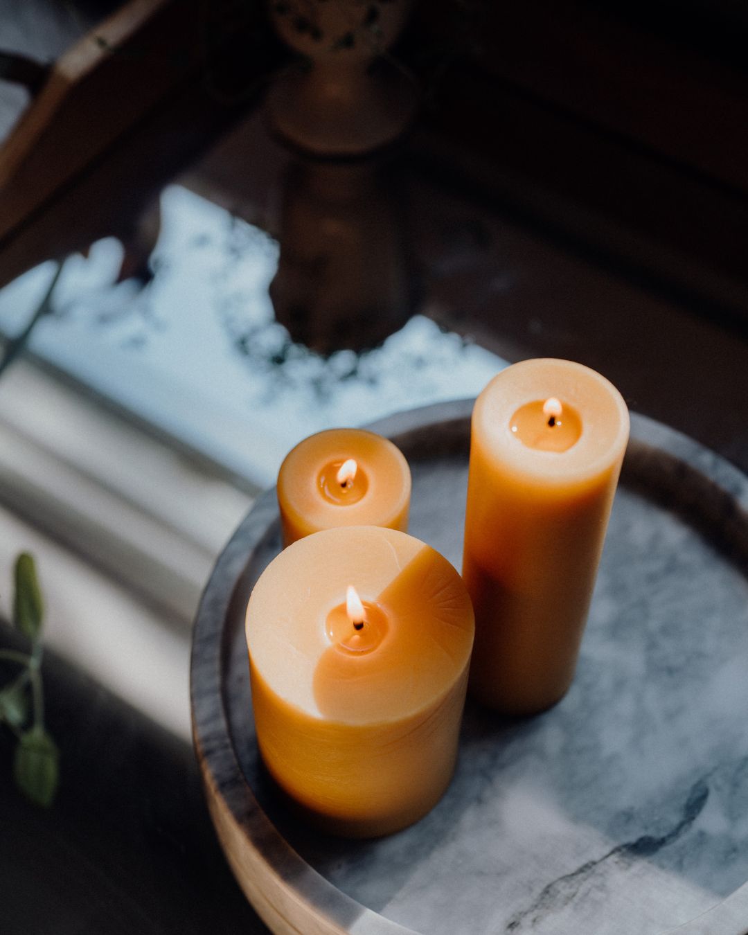 Three beeswax pillar candles on a marbled tray