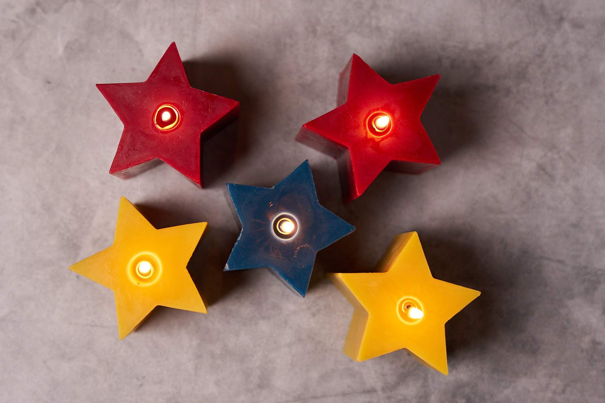Natural, red and blue five pointed star sculpted candles on a grey background.